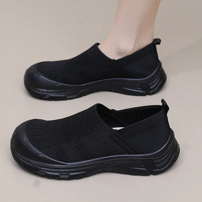 Women's one pedal slip-on shoe in black with cloth upper and PVC sole, showing round toe and flat heel design.