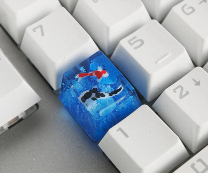 Close-up of a custom resin keycap featuring a detailed blue and orange koi fish scene, designed for Cherry MX mechanical keyboards.