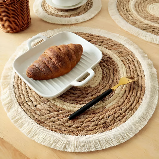 Round natural papyrus placemat with decorative tassels on a wooden dining table.
