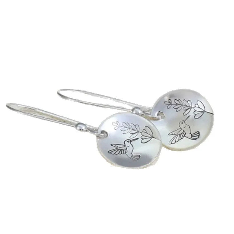 Close-up of women's silver retro earrings with glossy round bird and flower design.