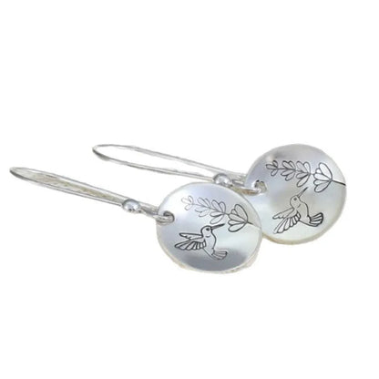 Close-up of women's silver retro earrings with glossy round bird and flower design.