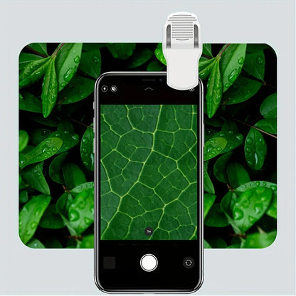 White mini mobile phone microscope with LED light and detachable clip-on adapter next to a smartphone.
