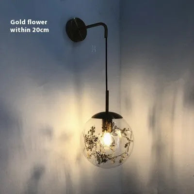 Glass wall lamp with golden flower finish and 15cm diameter, mounted beside bed with LED illumination