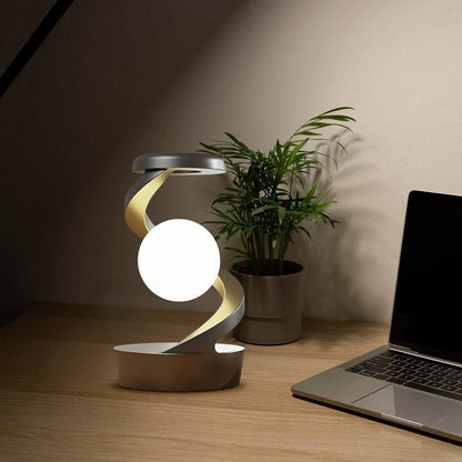 A rotating moon-shaped desk lamp with a wireless charging pad for smartphones, featuring a sleek and modern design.