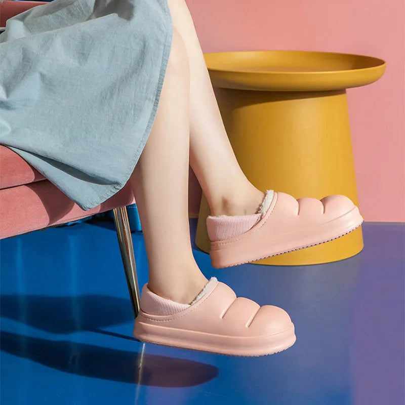 A pair of green waterproof EVA slippers with a plush lining and textured non-slip sole on a wooden floor.