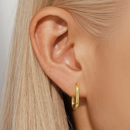 A pair of golden geometric clip-on earrings with a round design element on a white background.