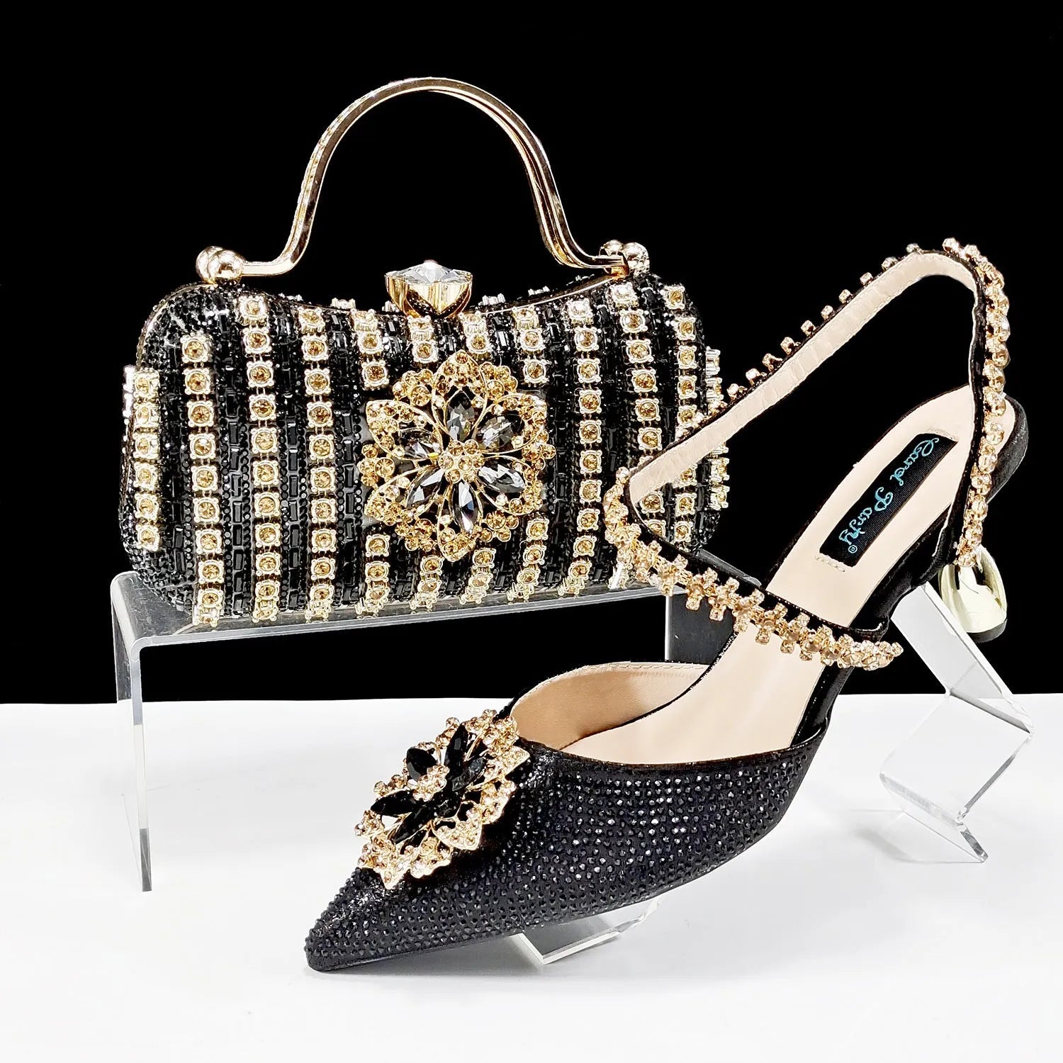 Women's black high-heel ankle strap shoes with floral rhinestone buckle and matching clutch bag on a neutral background