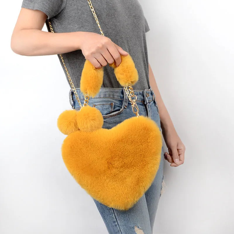 Women's plush handbag featuring a soft heart-shaped design with zipper closure and single adjustable shoulder strap, available in multiple solid colours including bean paste pink, watermelon red, and taro purple for daily wear and Valentine's Day styling.