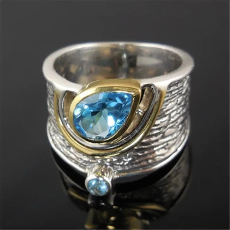 Close-up of a blue zircon drop-shaped alloy ring on a woman's finger, showing the inlaid stone setting.