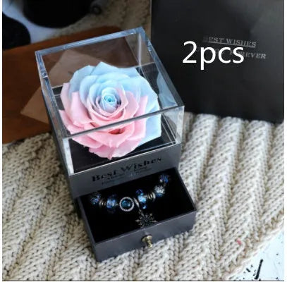 Blue and pink eternal flower gift box with roses and carnations on a table.