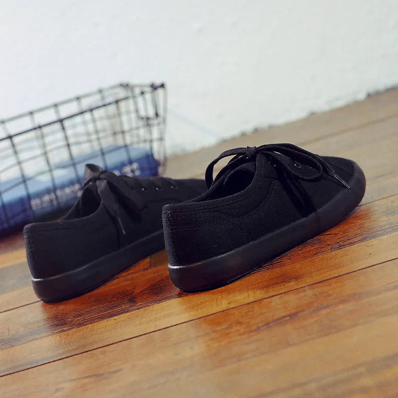 All-black women's canvas work shoes with flat rubber soles and lace-up front