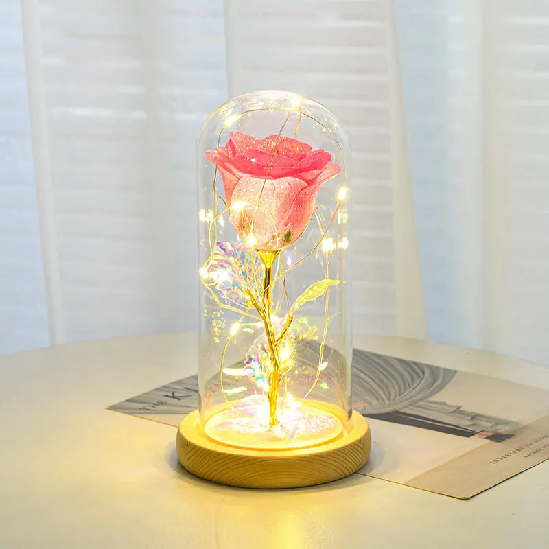Red eternal rose flower arrangement with LED lights inside a glass dome on a table.