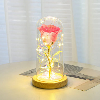 Red eternal rose flower arrangement with LED lights inside a glass dome on a table.