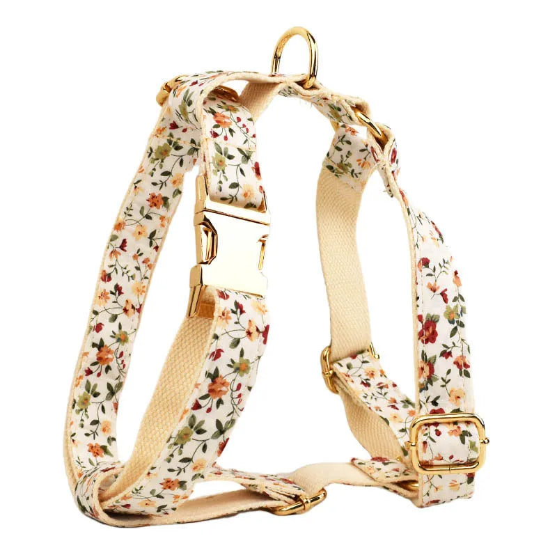 Small white flower patterned dog collar, leash, vest, bow, and poop bag holder set laid out flat.