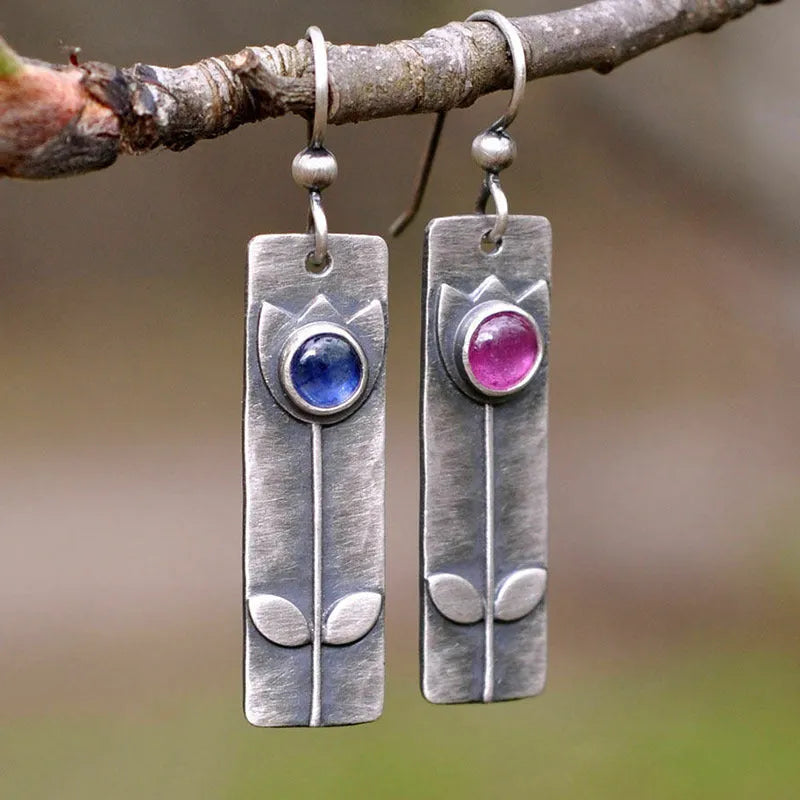 Geometric ellipse-shaped antique finish earrings with red sapphire stones on a white background.
