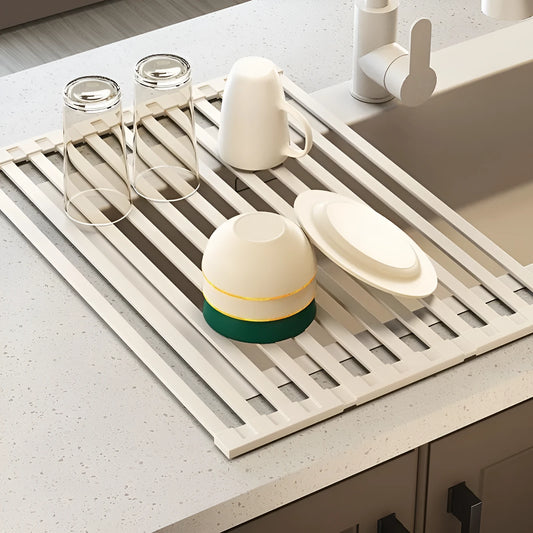 A milky white foldable stainless steel kitchen draining rack collapsed flat beside a kitchen sink.