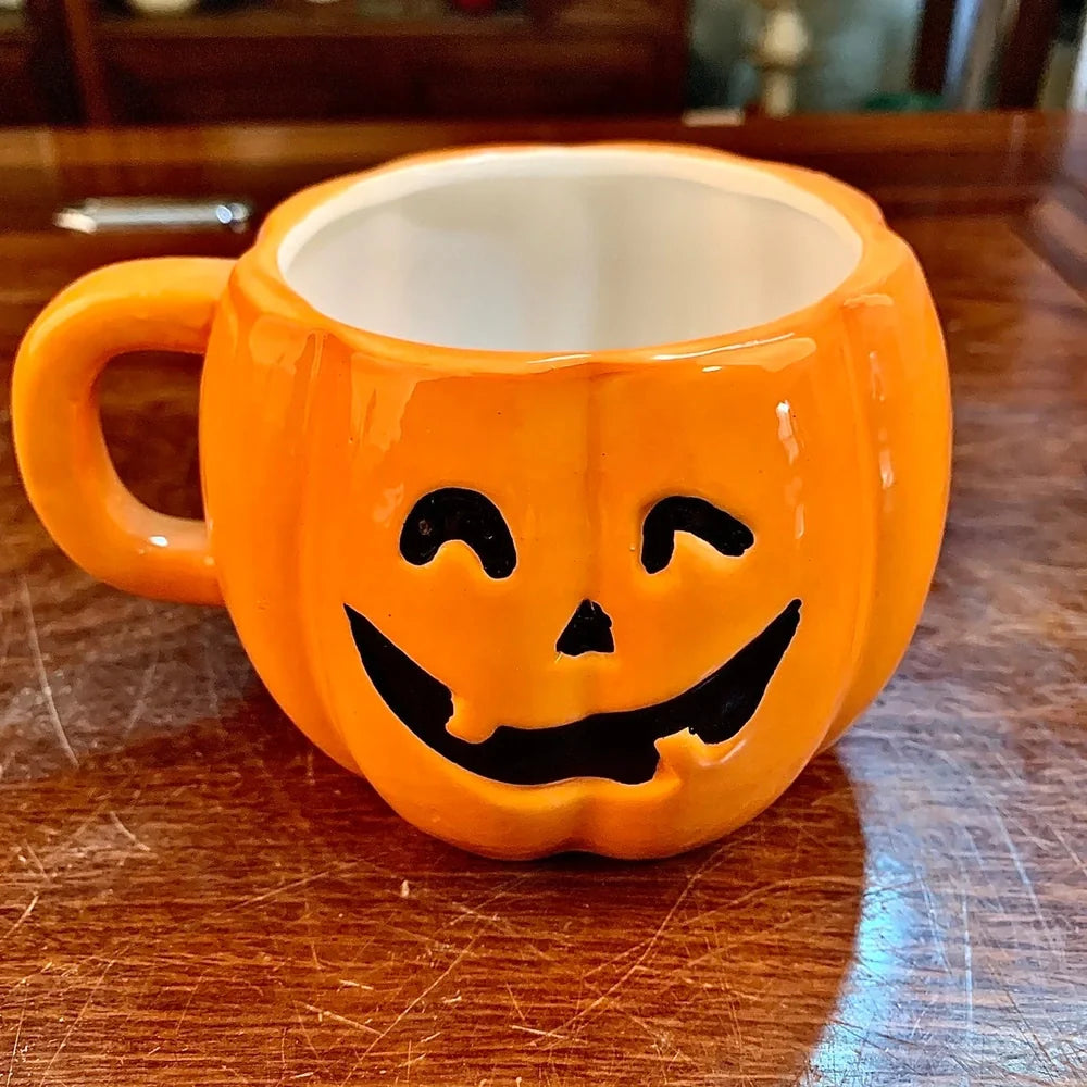 Orange ceramic Halloween pumpkin mug with cartoon face and included spoon on autumn table