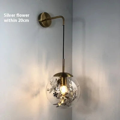 Glass wall lamp with golden flower finish and 15cm diameter, mounted beside bed with LED illumination
