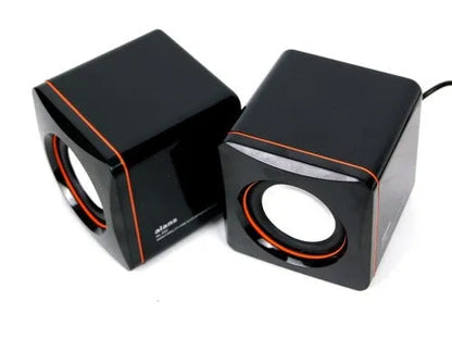 Black square USB computer speaker measuring 10cm with matte finish beside monitor