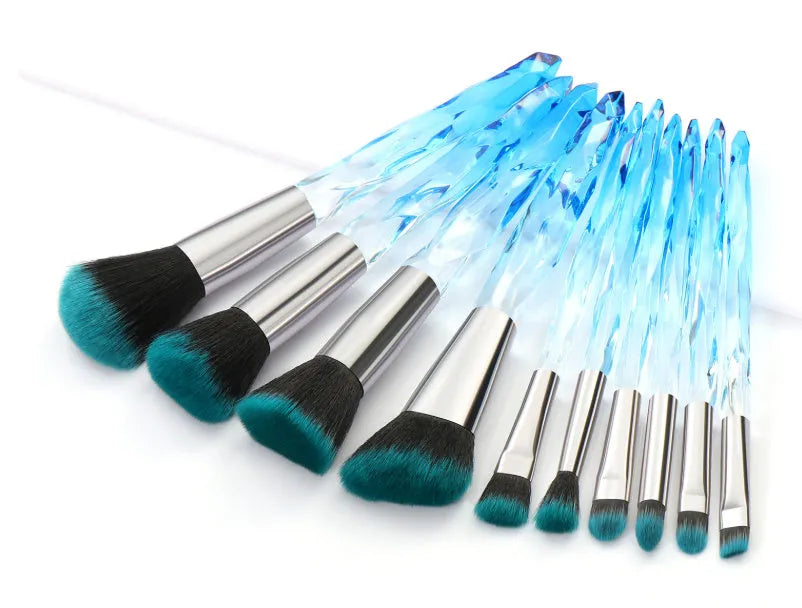 Ten clear crystal-handled foundation brushes with black synthetic bristles laid out on a surface.