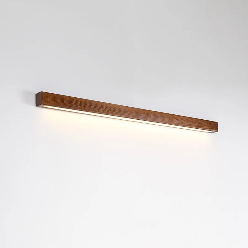 Walnut-coloured minimalist wooden strip wall lamp with integrated LEDs, mounted on a plain wall.