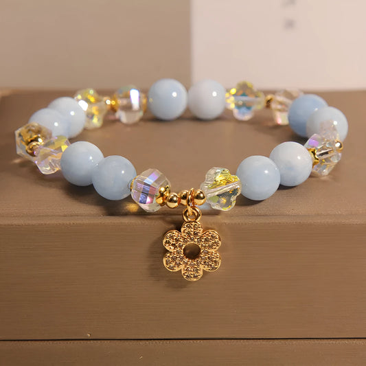 Women's aquamarine crystal four-leaf clover bracelet with pearl accents on wrist.