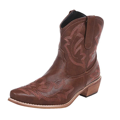 Women's brown embroidered ankle cowboy boots with a low wedge heel and pointed toe on a wooden floor.