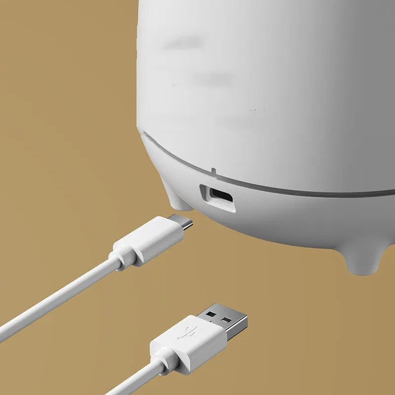 White volcano-shaped humidifier with USB cable on a wooden table, emitting mist.