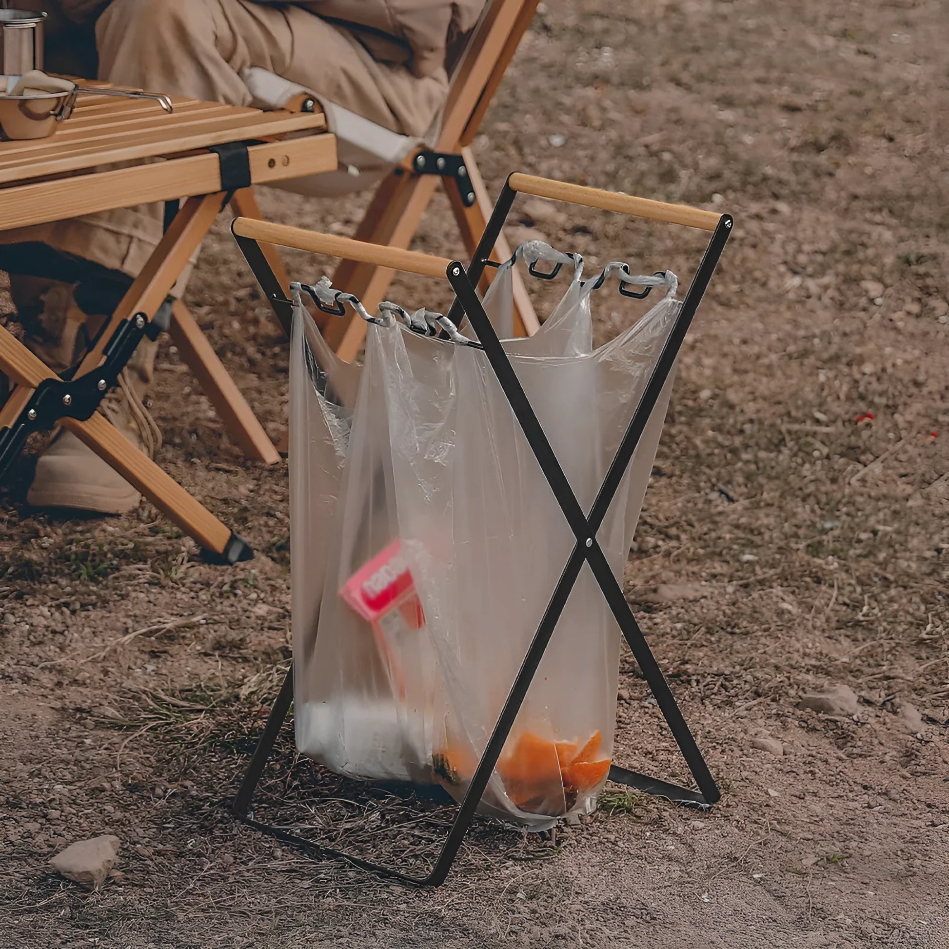 Black iron folding trash rack with wooden handles mounted on a wall holding a recycling bag.