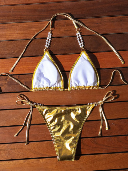 Gold women's halter neck bikini with lace-up front and pearl chain decoration on a solid background.