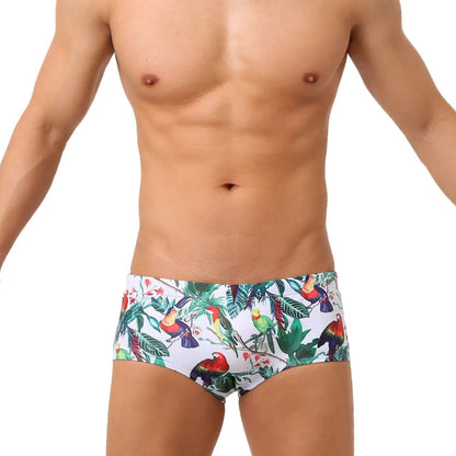 Men's blue swimming trunks with a detailed floral and bird print pattern, shown in a brief style.