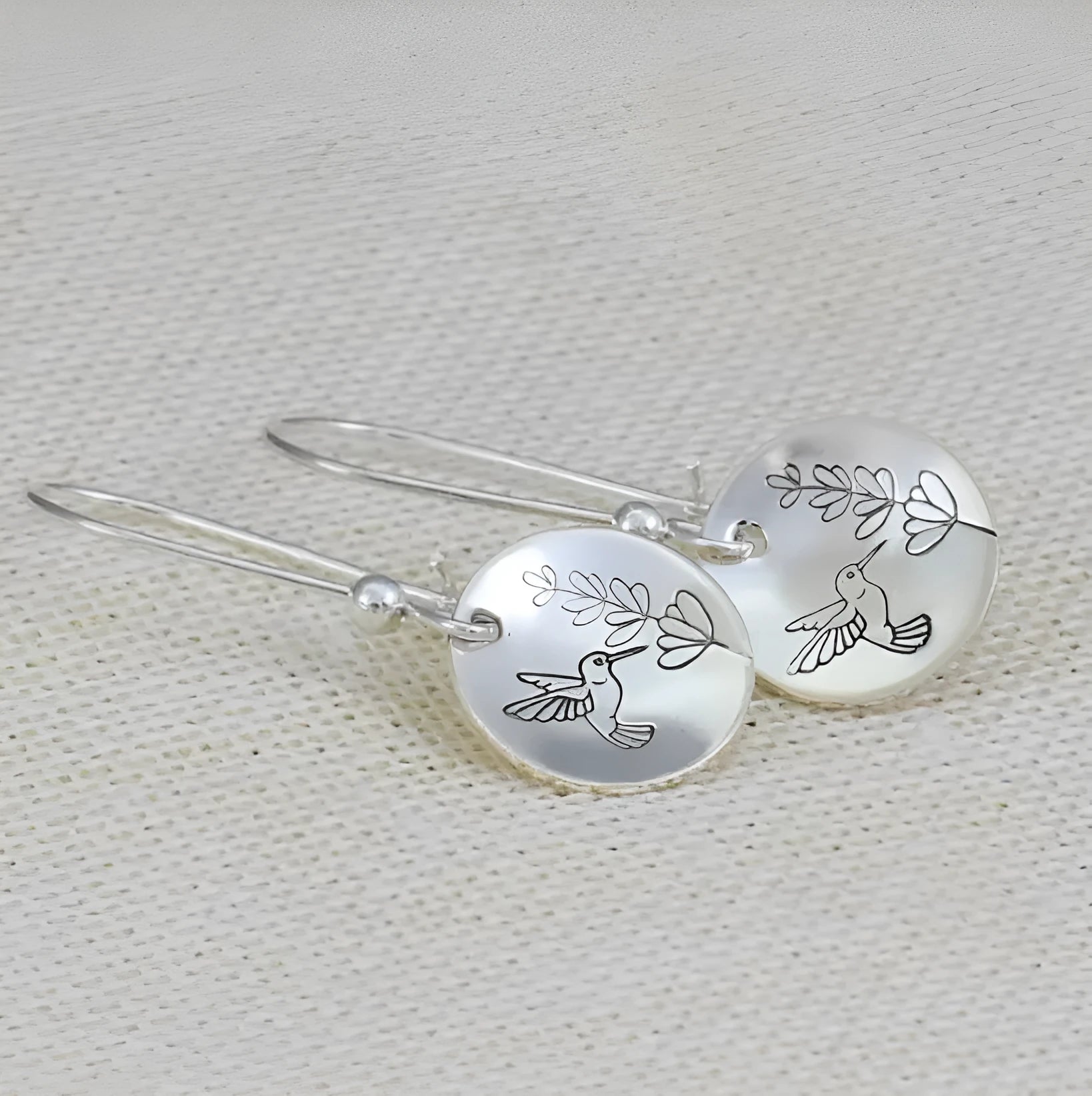 Close-up of women's silver retro earrings with glossy round bird and flower design.