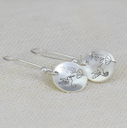 Close-up of women's silver retro earrings with glossy round bird and flower design.