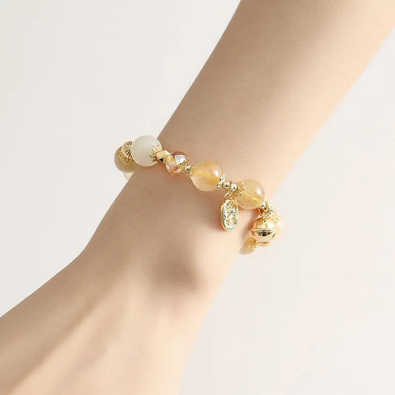 Gold-coloured rutilated quartz bracelet with a ringing bell charm on an adjustable band.