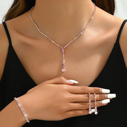 Women's silver pink rhinestone heart tassel earrings, necklace, and bracelet jewellery set on a white background.
