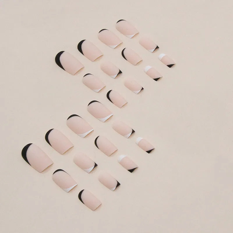 Set of 24 black and white frosted French tip fake nails with matte finish, laid out in size order.
