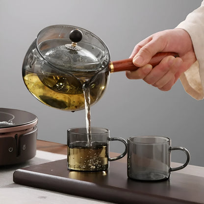 Glass teapot with wooden handle showing transparent borosilicate construction and removable infuser