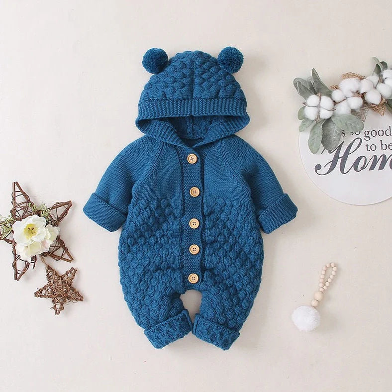 Baby wearing light blue knitted romper with hood and sleeveless design, single-breasted closure visible