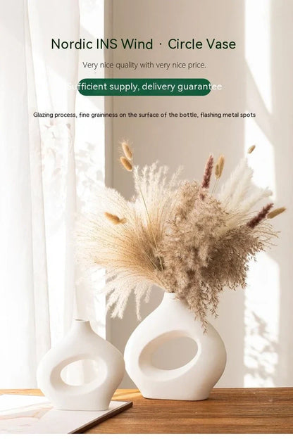 White ceramic circle vase with hand-painted coloured glaze on wooden table with dried flowers