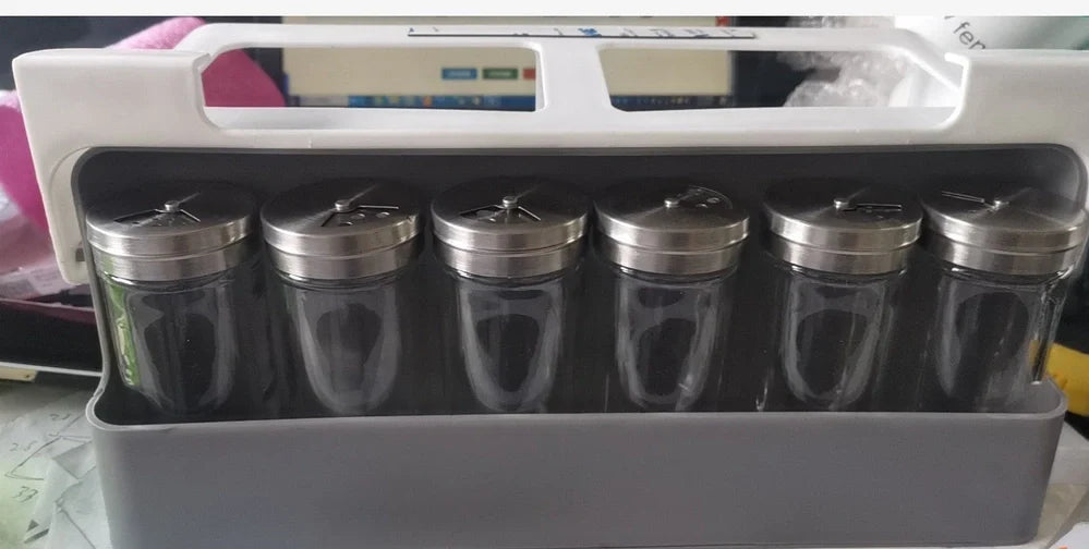 White plastic hanging spice rack with six clear glass bottles, mounted on kitchen door for punch-free storage