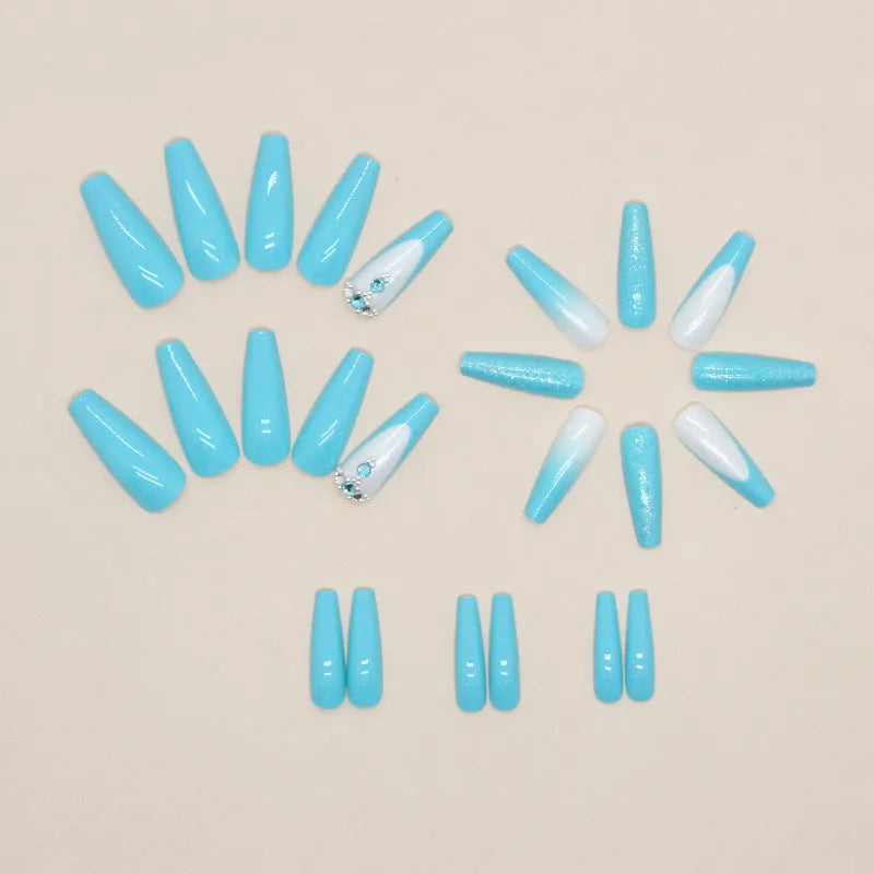 Set of long ballet-shaped false nails with smart blue colour and embedded diamond accents, next to a tube of adhesive glue.