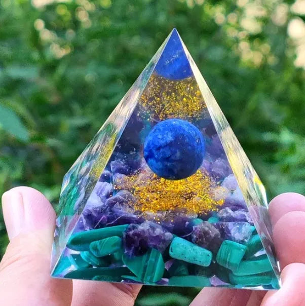 A small 6cm clear epoxy resin pyramid ornament containing pieces of natural crystal gravel on a flat surface.