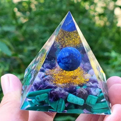 A small 6cm clear epoxy resin pyramid ornament containing pieces of natural crystal gravel on a flat surface.