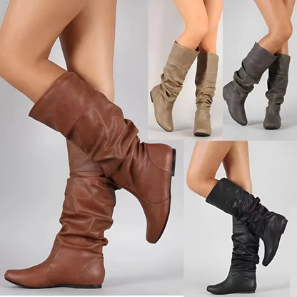 Women's flat slip-on boots in black with round toe and high cylinder shaft on a neutral background.