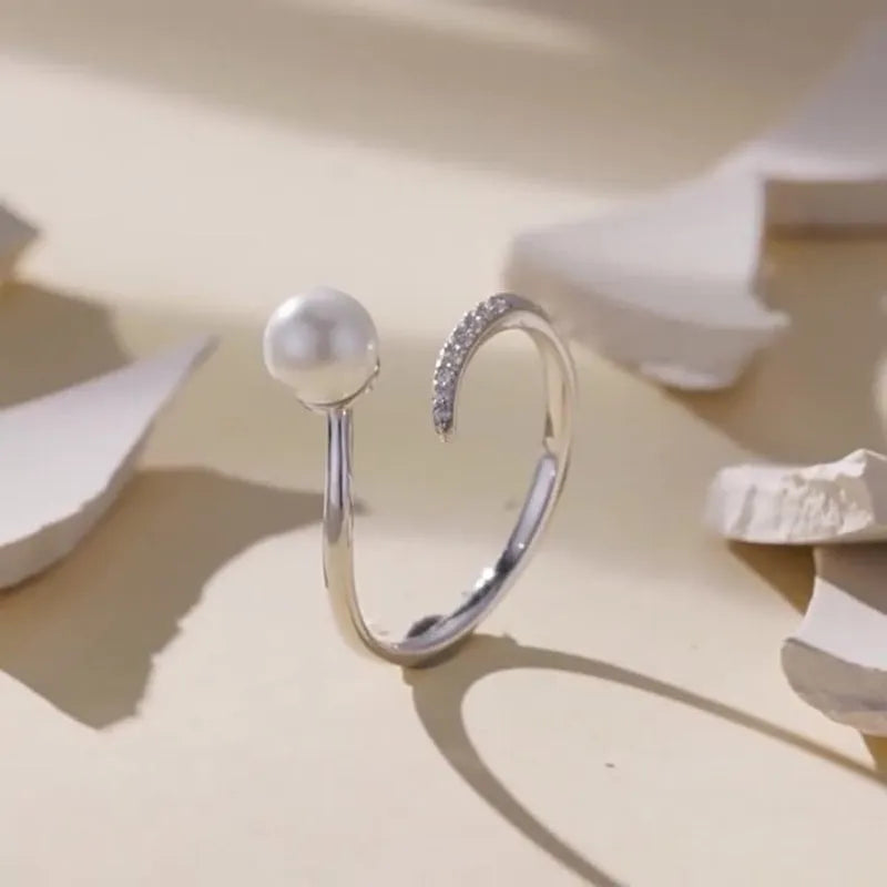 Silver adjustable open ring with white shell pearls on a white background.