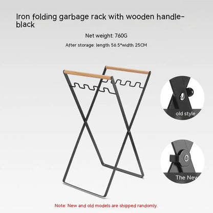 Black iron folding trash rack with wooden handles mounted on a wall holding a recycling bag.