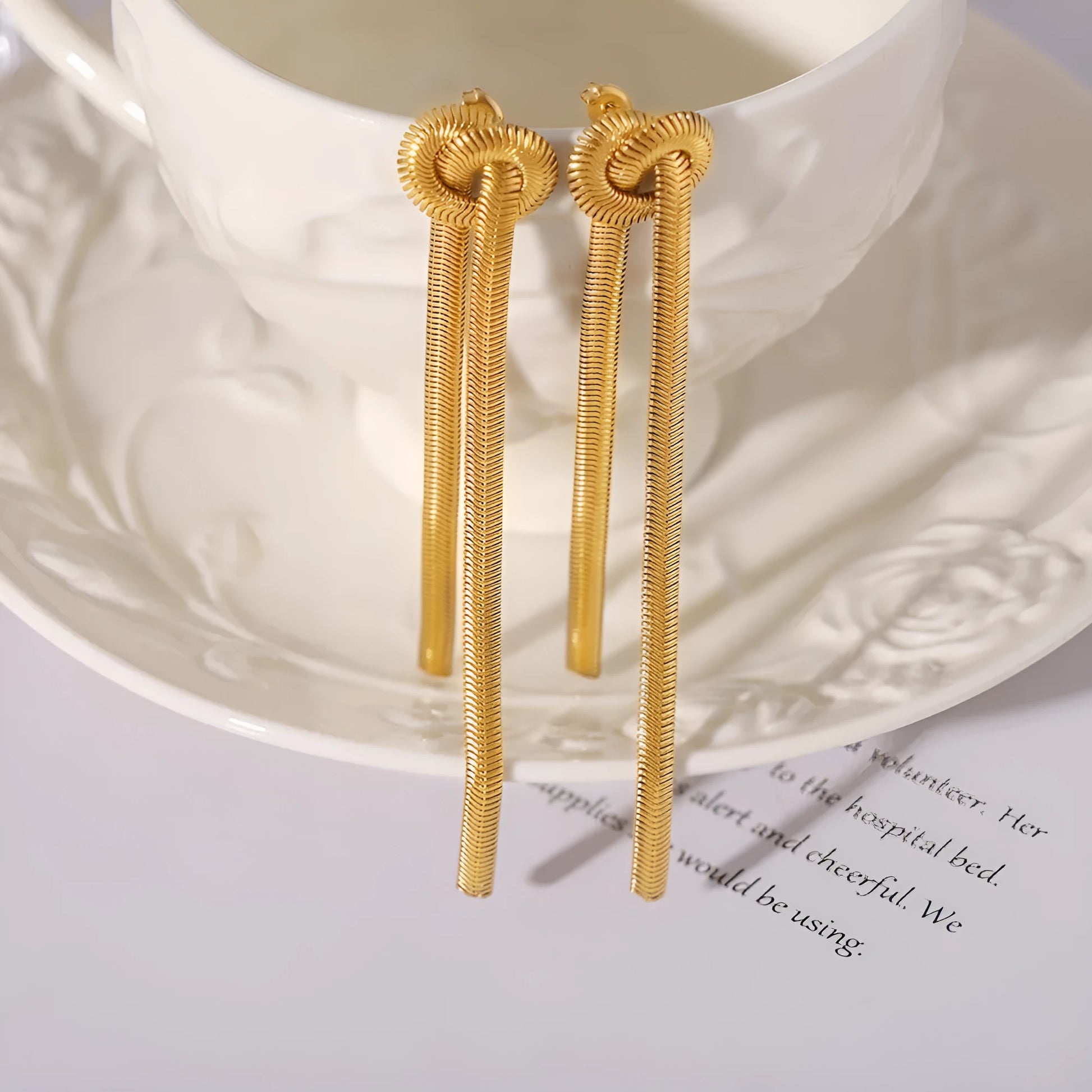 Gold electroplated titanium steel knotted tassel necklace and matching earrings set on a white background.