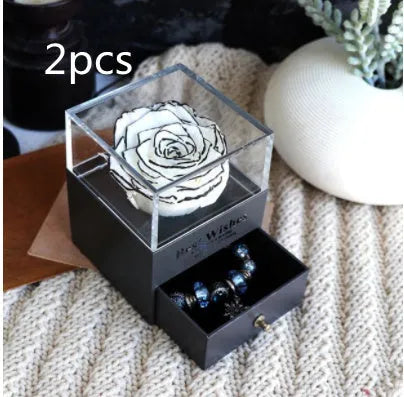 Blue and pink eternal flower gift box with roses and carnations on a table.