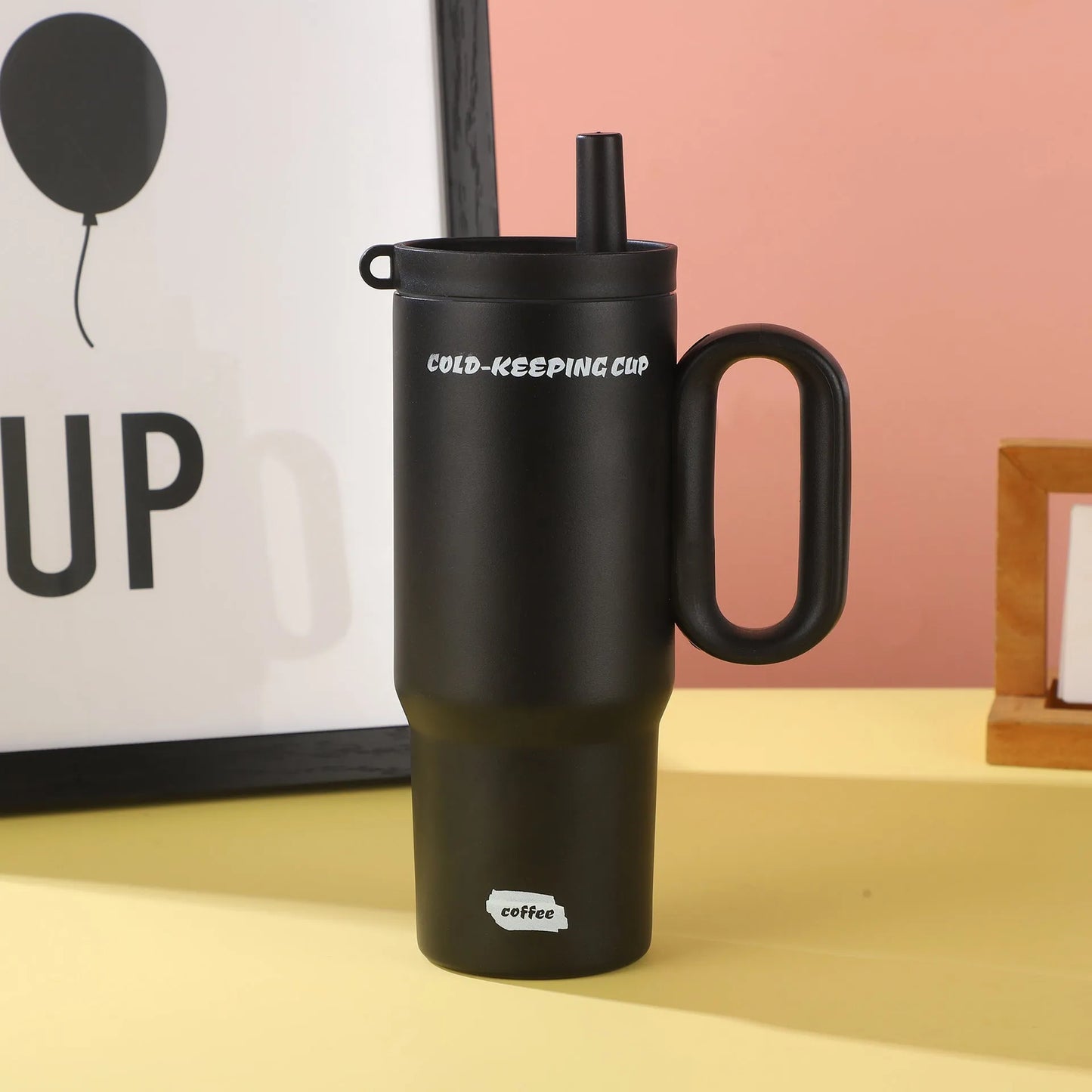 Large pink insulated straw cup with a black handle and push-button lid on a wooden table