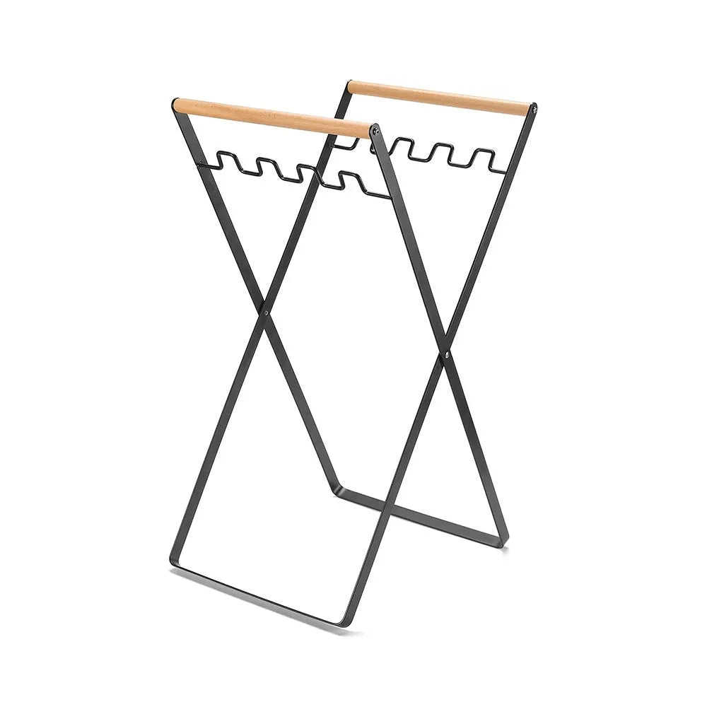 Black iron folding trash rack with wooden handles mounted on a wall holding a recycling bag.